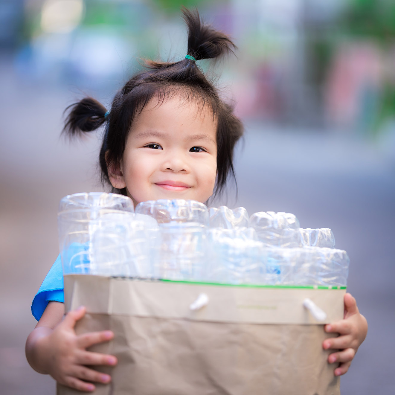 Little girl holding a bag of plastic water bottles for recycling